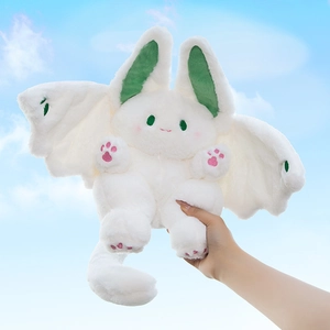 Cute white bat bunny plush toy with green wings held against a bright blue sky background
