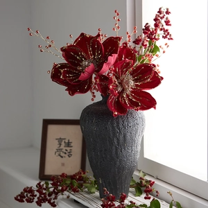 Red Christmas faux flowers with gold trim in a minimalist matte black ceramic vase