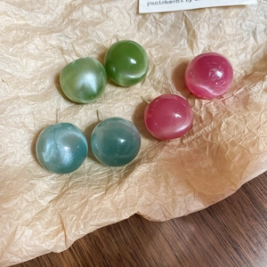 Detail of round candy-colored earrings in green, rose, and blue-gray on paper