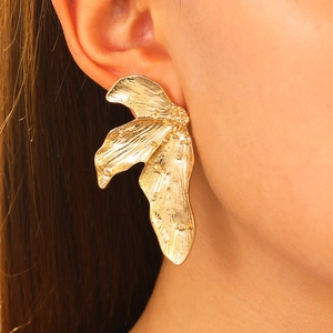Macro detail of golden oversized irregular leaf earrings with hammered texture on model