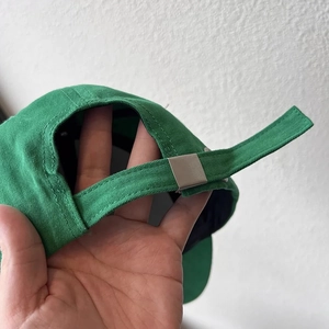 Detail of adjustable metal buckle and canvas strap on dark green baseball cap
