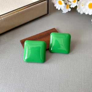 Detailed view of vintage square green resin stud earrings on a minimalist wooden base