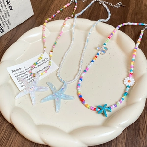 Detail of colorful beaded necklaces with starfish and daisy pendants on a ceramic tray