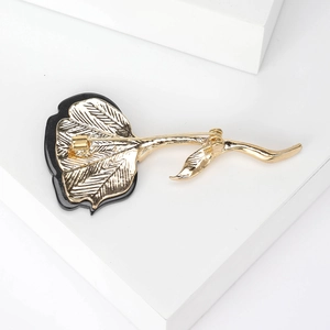 Elegant gold and black flower brooch with metal pin backing shown on a white pedestal