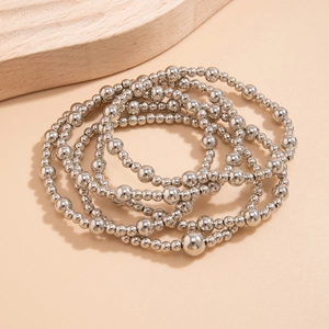 Close-up of a silver multi-layer beaded bracelet with a heart pendant on a neutral base