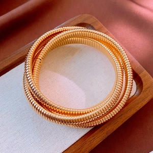 Gros plan d'un bracelet spirale doré multicouche sur plateau en bois et tissu soie