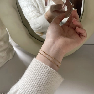 Close-up of a double-layer gold beaded bracelet with a minimalist polished square charm