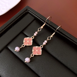 Dettaglio degli orecchini pendenti in oro rosa con fiori di smalto su pelle nera