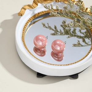 Detailed view of pink faux pearl earrings on a round mirror with dried flower accents