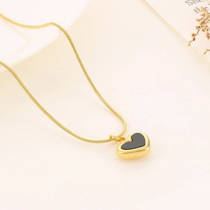 Macro detail of a gold heart pendant necklace with black inlay on a beige surface