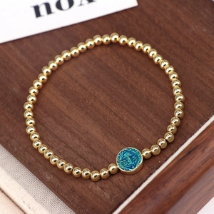 Macro detail of gold beaded bracelet with a blue enamel religious Virgin Mary medal