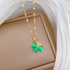 Macro detail of gold clover necklace with green stone and zircon heart on silk background