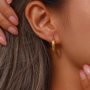 Close-up of gold-plated hoop earrings featuring elegant diagonal stripe textures on a model