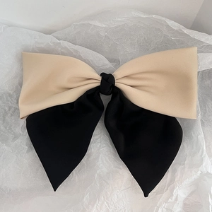 Close-up of a two-tone beige and black satin bow hair clip on a textured white background