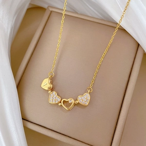 Detail of a gold clover necklace with heart-shaped crystal charms on a silk background