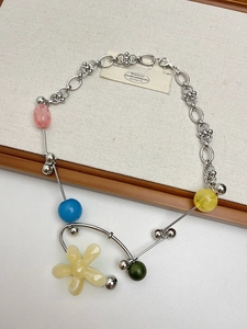 Detail of silver chain necklace with colorful beads and beige flower pendant on fabric