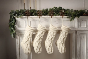 Close-up of four cream cable-knit Christmas stockings hanging on a white festive fireplace