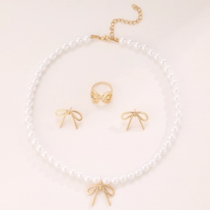 Flat lay of vintage bow jewelry set featuring pearl necklace, earrings and ring in gold finish