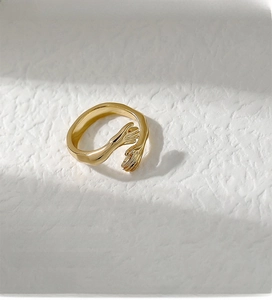 Macro shot of gold adjustable hugging hands ring on textured white background