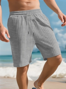 Detail view of men's grey striped knit shorts with drawstring on a sunny beach