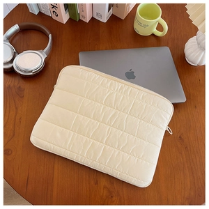 Quilted laptop sleeve in cream white on a dark wooden desk with office accessories