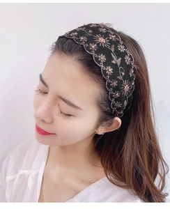Detalle de diadema ancha negra con bordado floral dorado sobre tela de calidad