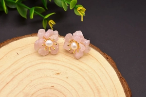 Macro detail of pink flower earrings with pearl center on a natural wood base