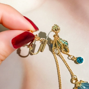 Detail of adjustable gold spiral ear clip with blue rhinestones and shell tassel pendant