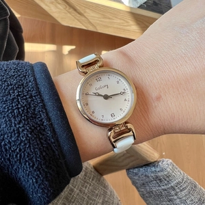 Close-up of a women's watch with white leather strap and gold case on wrist