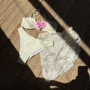 Close-up of cream ribbed bikini set with white floral lace beach cover-up on straw mat