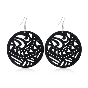 Detail of black hollowed-out wooden earrings with tribal geometric patterns and metal hooks