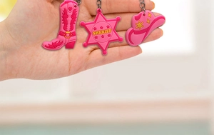 Close-up of pink silicone cowboy boot, sheriff badge, and hat charms with metal keychains