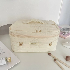 Detailed view of cream quilted makeup bag with bunny embroidery on a white desk setup