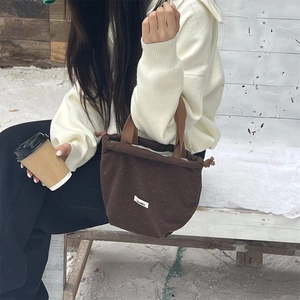 Close-up of brown wool drawstring bucket bag with white polka dots and logo label