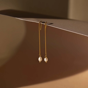 Artistic close-up of gold 18K plated baroque pearl threader earrings on beige paper