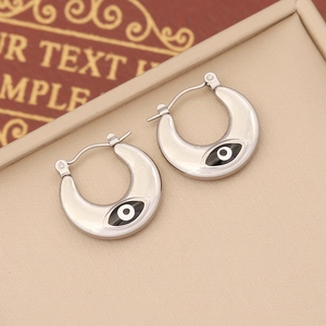 Macro shot of silver crescent evil eye earrings resting on a beige jewelry display stand