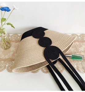 Detailed close-up of woven straw tote bag with black accents on a white lace background