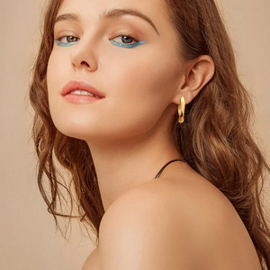Close-up of elegant 18K gold twisted hoop earrings worn by a model with stylish blue eyeliner