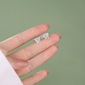 Minimalist S925 sterling silver butterfly stud earrings displayed on a finger for scale
