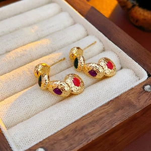 Macro shot of vintage gold earrings with green and purple gemstones in a beige velvet box