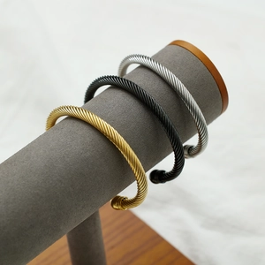 Three men's stainless steel cable bracelets in gold, black, and silver on a velvet display