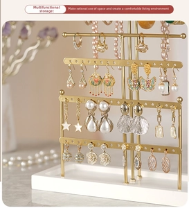 Detail of 6-tier gold metal earring stand with jewelry on white marble base