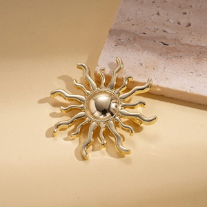 Macro view of a polished gold sunburst brooch with wavy rays on a stone surface
