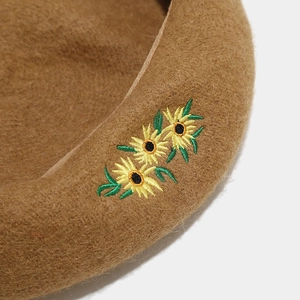 Makroaufnahme von Sonnenblumen-Stickerei und Wolltextur auf einer khaki Baskenmütze