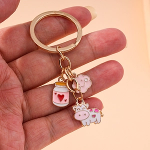 Golden keychain with pink cow, milk bottle and cloud pendants on a soft pink backdrop