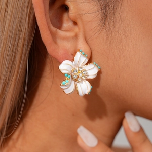 Detailed close-up of a white flower earring with gold edges and blue crystal beads