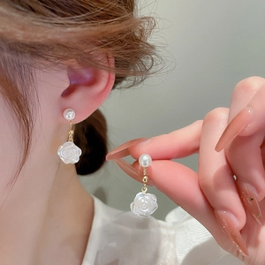 Close-up of white flower and pearl earrings in gold finish on female model