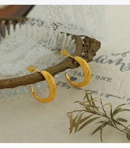 Detail of 18K gold plated C-shaped earrings with hammered texture on a glass tray