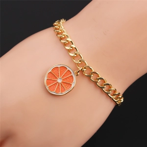 Detailed view of a gold chain bracelet with a realistic orange slice enamel charm on a model