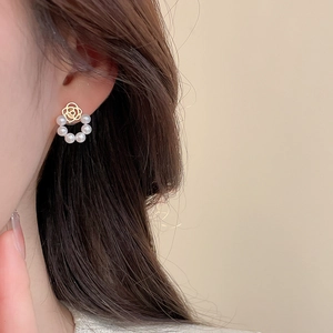 Detailed view of elegant gold rose and pearl drop earrings worn by a model in soft light